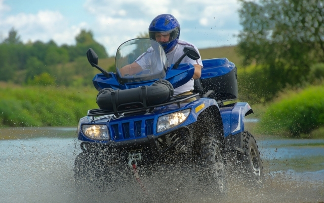 A man riding on an ATV across water in an outdoor setting.