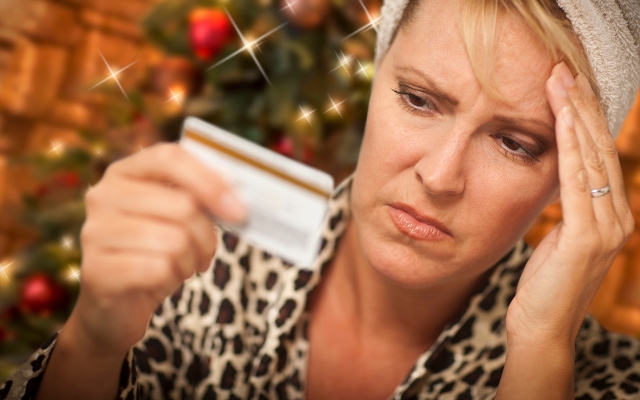 A woman looking stressed with her credit card in hand and Christmas decorations in the background