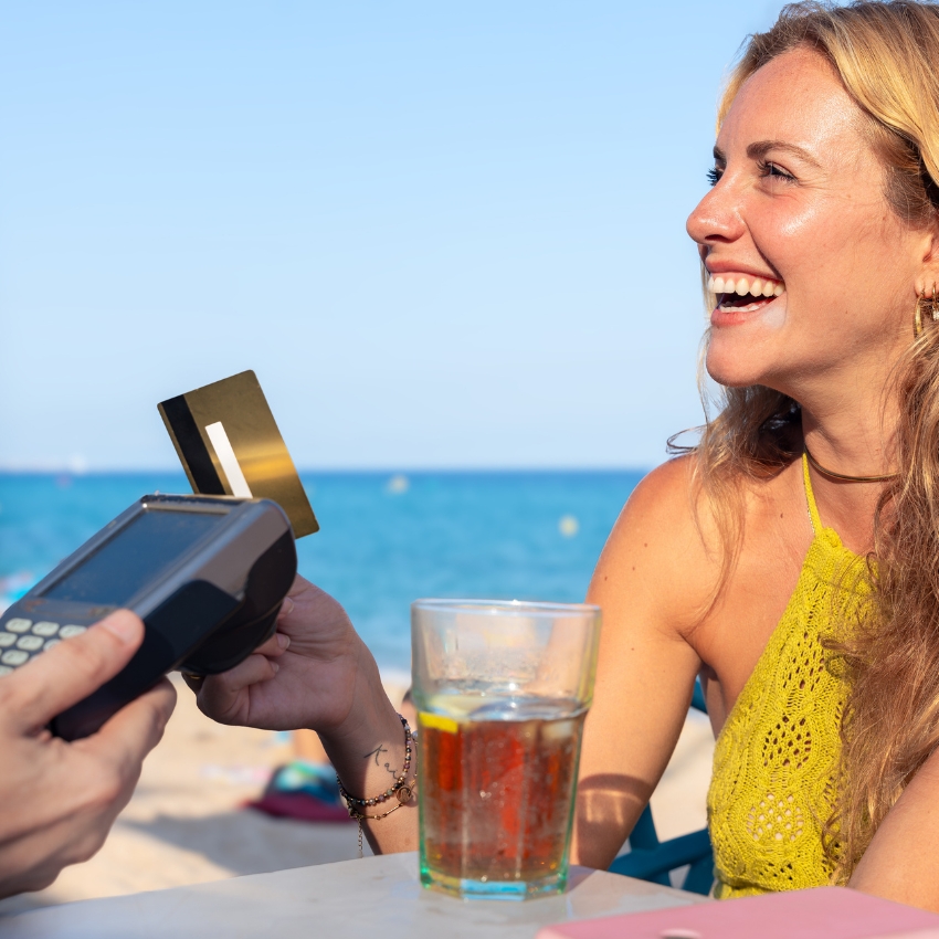woman smiling on a beach holding a credit card